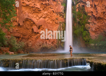 USA, Arizona, Havasu Canyon. Une femme en bikini patauge dans le ruisseau en aval thundering Mooney Falls. (MR) Banque D'Images