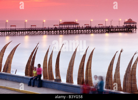 Le Pérou, La Libertad, Huanchaco. Scène au bord de l'eau à Huanchaco au nord du Pérou, où les habitants se détendre à côté de Totora (roseaux) bateaux empilés le long de la plage. Banque D'Images