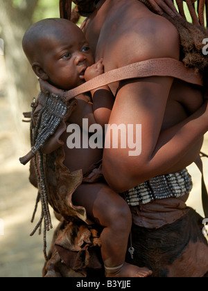 La Namibie, Kaokoland. Un enfant se fait sur le dos de sa mère dans un cuir magnifiquement décorées. Le corps d'une femme est smeare Banque D'Images