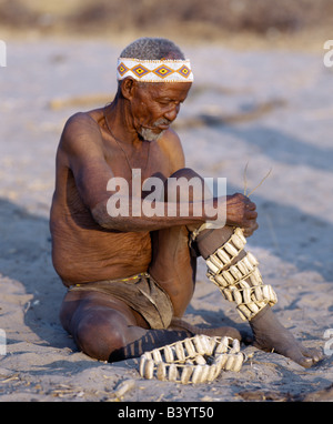 La Namibie, l'Est Bushmanland, Tsumkwe. Un vieil homme !Kung cloches en bois sangles aux jambes en préparation d'une danse. Les !Kung sont Banque D'Images