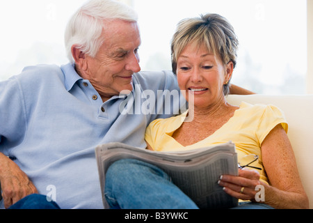 Dans la salle de séjour couple reading newspaper smiling Banque D'Images