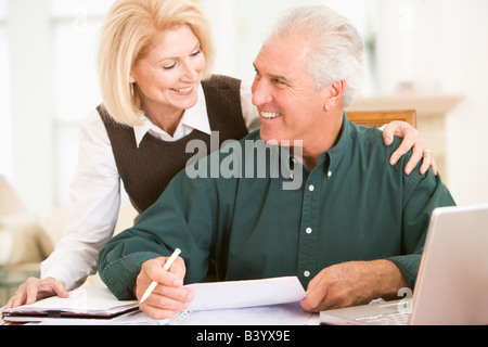 Couple dans la salle à manger avec un ordinateur portable et de la paperasserie smiling Banque D'Images