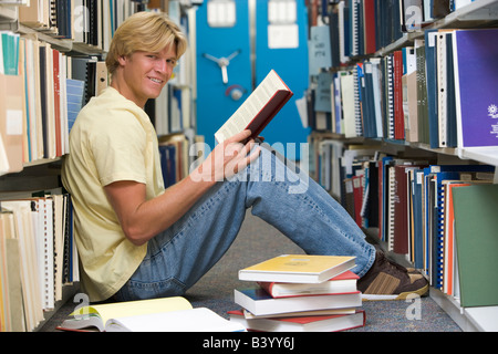 Man sitting on floor in library holding book Banque D'Images