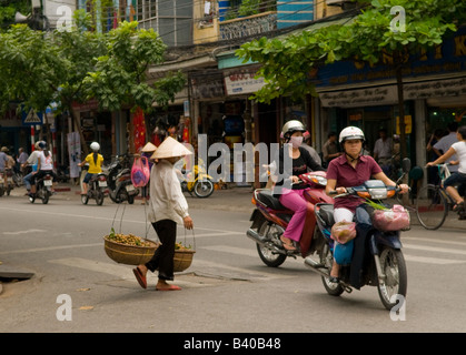 Une vietnamienne portant des fruits sur son épaule en traversant la rue, Hanoi, Vietnam Banque D'Images