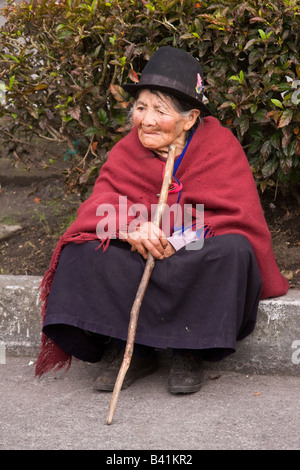 Personnes âgées Quechuan femme portant un costume traditionnel avec un bâton de marche assis sur un trottoir en Équateur Banos Banque D'Images