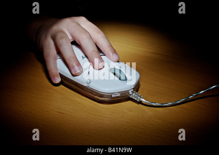 La main de l'enfant tenant une souris d'ordinateur sur une table en bois Banque D'Images