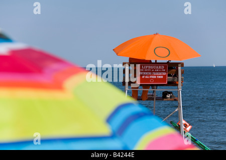 Un sauveteur à l'abri du soleil d'été sous un parapluie orange. Banque D'Images