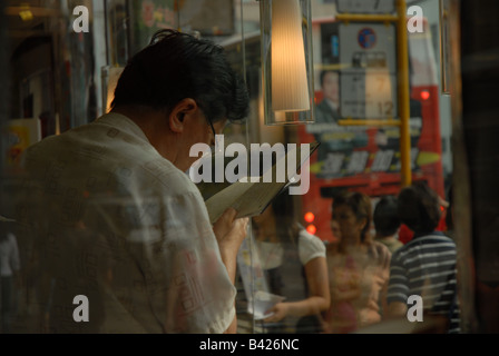 Un homme lit à côté d'une fenêtre dans un café à Hong Kong Banque D'Images