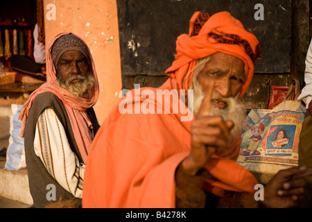 Un homme d'âge mûr avec une barbe se trouve sur un mur dans la ville de Varanasi, en Inde. Un sadhu porter du rouge se trouve au premier plan. Banque D'Images