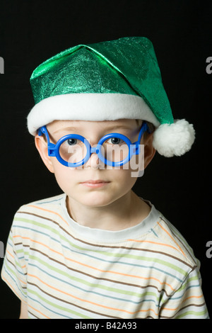 Un jeune garçon avec un chapeau de sorcière vert, bleu et blanc lunettes tassle ; portrait isolé sur un fond noir. Banque D'Images