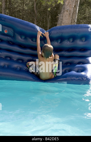 Un jeune garçon tente d'activer plus d'un lilo dans la piscine Banque D'Images