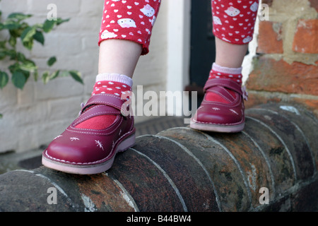 Jeune fille en équilibre sur un mur de jardin, le port de chaussures en cuir rouge neuf Banque D'Images