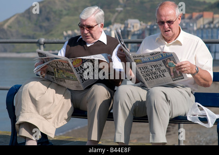Deux hommes d'âge moyen assis sur un banc au bord de la mer lire le Daily Mail et le Daily Express tabloïdes Aberystwyth UK Banque D'Images