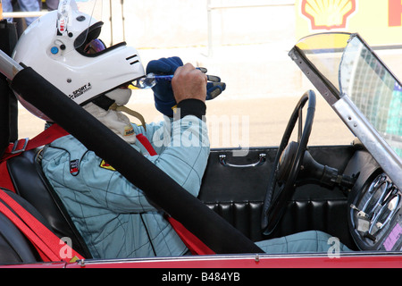 Voiture de course rouge classique avec le pilote verre avant la course encore portant un casque blanc Banque D'Images