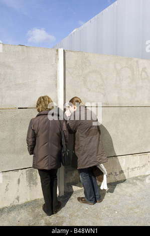 Deux femmes regardant à travers une fente dans le reste du mur de Berlin, Allemagne Banque D'Images