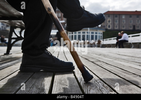 Un homme âgé avec bâton de marche assise sur un banc sur un quai Banque D'Images