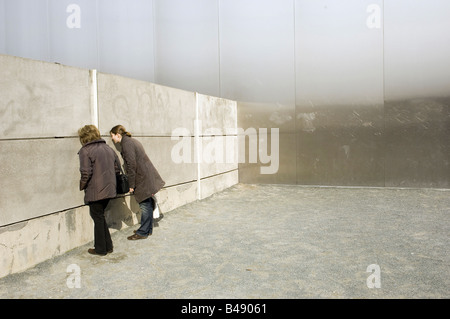 Deux femmes regardant à travers une fente dans le reste du mur de Berlin, Allemagne Banque D'Images