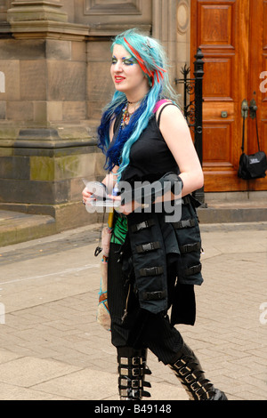 Edinburgh Fringe Festival punk girl en noir , long cheveux bleu et rouge , body piercing & bouclée bottes à voler pour feuilles montre Banque D'Images