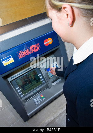 Young businesswoman in suit l'insertion de carte dans un guichet automatique machine point de trésorerie Lien UK Banque D'Images