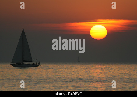 Un petit yacht navigue à travers la partie rouge du coucher du soleil à Aberystwyth, Ceredigion, pays de Galles Banque D'Images