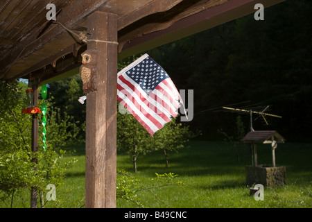 Un drapeau américain en lambeaux s'agite dans la brise sur le porche d'une vieille maison de bois, avec des ornements du vent derrière. Banque D'Images