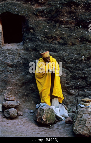 Scène tôt le matin à Lalibela Ethiopie,. Un prêtre se tient près de sa petite grotte chambre et lit la bible. Banque D'Images