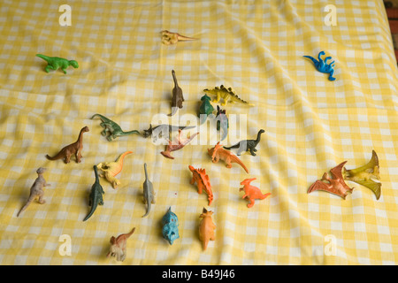 Bouquet coloré de dinosaures jouets en plastique bon marché se trouvent dispersés sur un tissu blanc et jaune à carreaux après une bataille de titans Banque D'Images