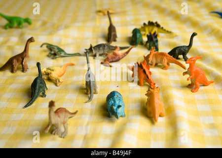 Bouquet coloré de dinosaures jouets en plastique bon marché debout sur un tissu blanc et jaune à carreaux avant une bataille de titans Banque D'Images