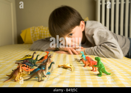 Un pré-ado garçon regarde sur une horde de dinosaures en plastique coloré organisé en rangs de bataille avec un Diplodocus abattus entre eux Banque D'Images