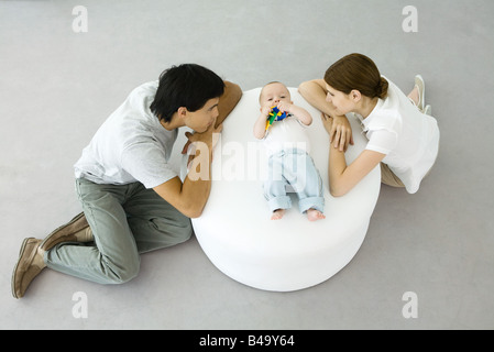 Les jeunes parents appuyé contre un pouf, regardant bébé couché entre eux