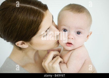 Mère embrassant bébé sur la joue, baby looking at camera Banque D'Images