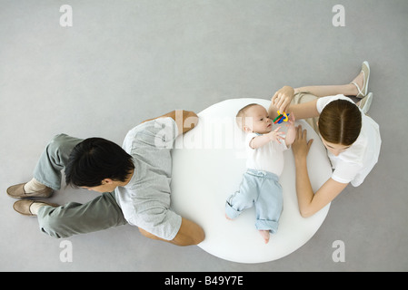 Mère jouer avec bébé couché sur un pouf, père assis avec dos tourné à eux, overhead view