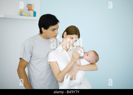 Mère de nourrir bébé avec une bouteille, mari de regarder par-dessus son épaule Banque D'Images