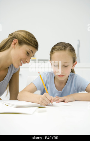 Girl doing homework at table, mère regardant Banque D'Images