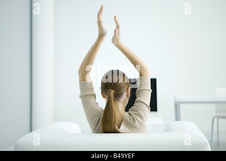 Femme regardant la TV, bras levés en l'air, vue arrière Banque D'Images