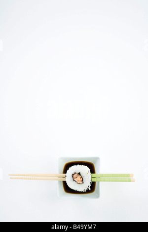 Seule Pièce de maki sushi sur baguettes sur le plat de la sauce de soja, overhead view Banque D'Images