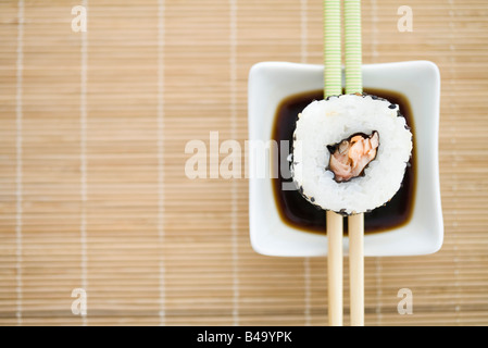 Seule Pièce de maki sushi reposant sur des baguettes sur la sauce, overhead view Banque D'Images