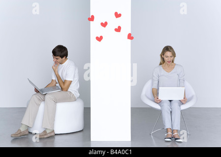 L'homme et la femme l'utilisation d'ordinateurs portatifs, coeurs flottant dans l'air entre eux Banque D'Images