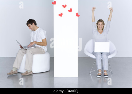 L'homme et la femme l'utilisation d'ordinateurs portatifs, coeurs flottant entre eux, woman's arms Banque D'Images