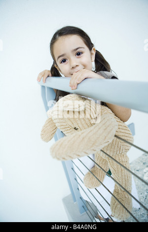 Petite fille debout à rail holding teddy bear, smiling at camera Banque D'Images