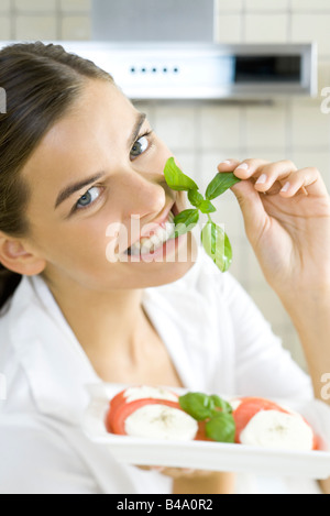 Woman biting en brin de basilic, la plaque de salade caprese Banque D'Images