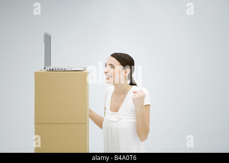 Woman smiling with hands raised, looking at laptop computer placées haut sur boîte en carton Banque D'Images