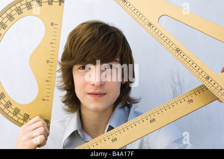 Jeune homme tenant divers instruments de mesure, smiling at camera Banque D'Images