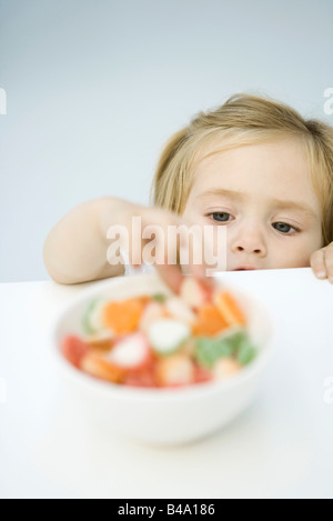 Bébé fille atteindre pour bol de bonbons Banque D'Images