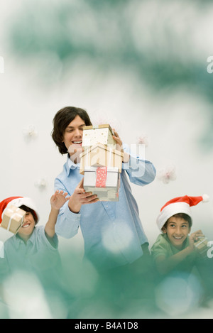 Young man holding pile de cadeaux, boys wearing Santa hats attraper cadeaux chute Banque D'Images