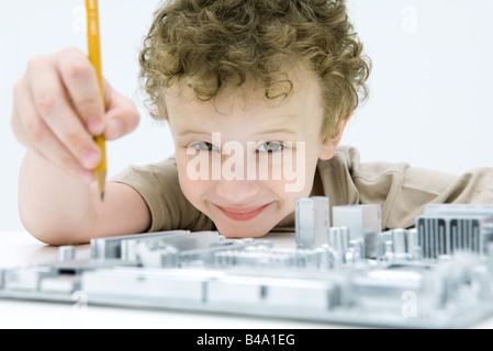 Little Boy holding pencil sur carte mère de l'ordinateur, smiling at camera Banque D'Images