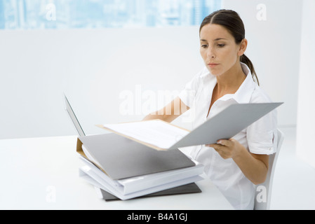 Femme assise au bureau, à la recherche de classeurs empilés Banque D'Images