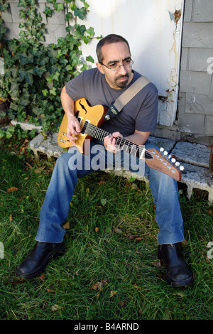 Portrait de l'environnement d'un homme d'origine ethnique hispanique qui joue de la guitare. Il est assis et porte une chemise grise jeans et bottes Banque D'Images