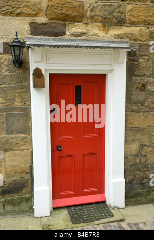 Une porte rouge vif sur un chalet traditionnel à Robin Hood's Bay, North Yorkshire, Angleterre Banque D'Images