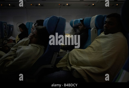 Cabine avec lumières tamisées les passagers en classe économique dormir sous des couvertures sur un vol long-courrier international Banque D'Images